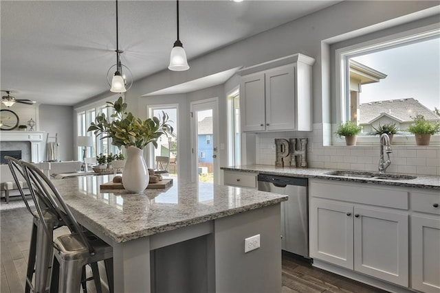 kitchen featuring stainless steel dishwasher, a center island, a sink, decorative backsplash, and dark wood finished floors