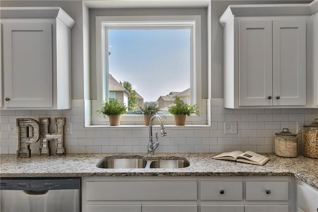 kitchen featuring a sink, dishwasher, white cabinets, backsplash, and light stone countertops