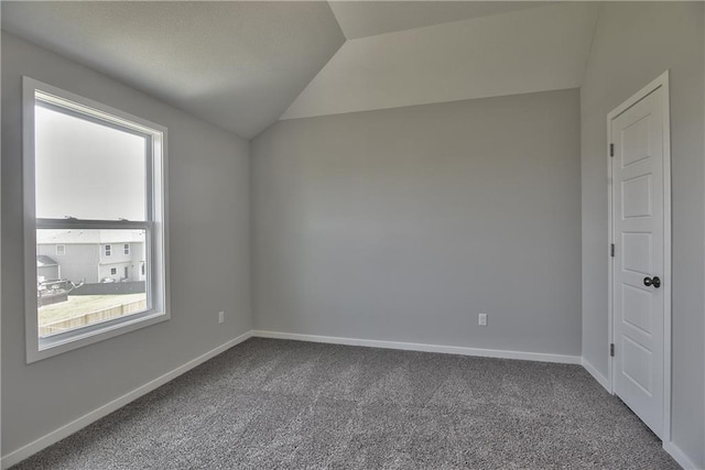 carpeted empty room featuring vaulted ceiling and baseboards