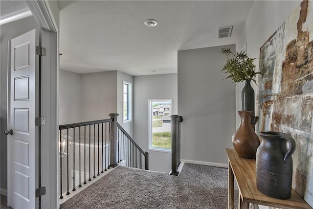 hallway featuring a textured ceiling, an upstairs landing, carpet floors, baseboards, and visible vents