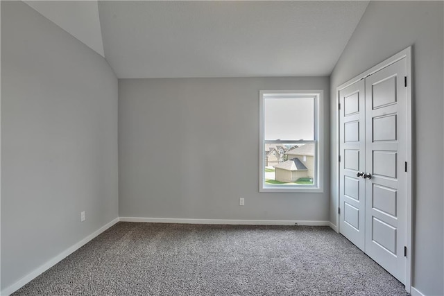 carpeted spare room featuring vaulted ceiling and baseboards