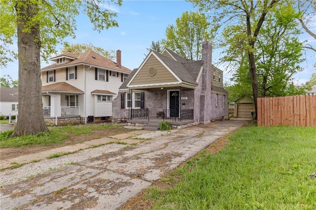 view of front of property featuring fence, brick siding, a detached garage, covered porch, and driveway