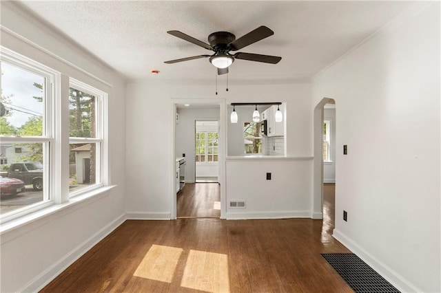 unfurnished room featuring arched walkways, visible vents, a wealth of natural light, and wood finished floors