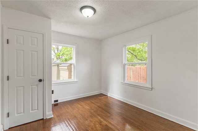 spare room with dark wood-type flooring, a textured ceiling, baseboards, and a healthy amount of sunlight
