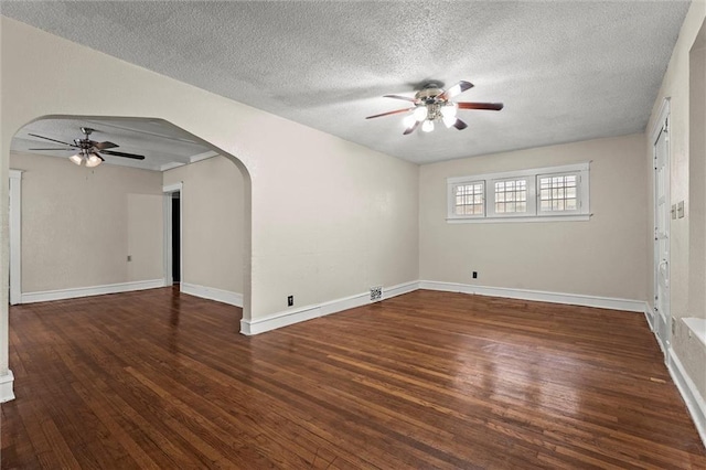 empty room with wood finished floors, baseboards, ceiling fan, a textured ceiling, and arched walkways