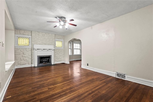 unfurnished living room with ceiling fan, arched walkways, a textured ceiling, a fireplace with flush hearth, and wood finished floors