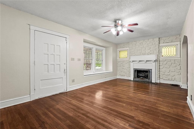 unfurnished living room featuring wood finished floors, baseboards, ceiling fan, a textured ceiling, and a fireplace with flush hearth