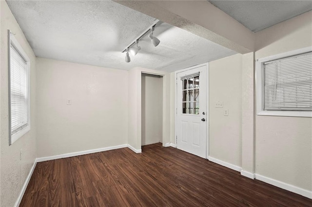 spare room featuring baseboards, rail lighting, a textured ceiling, and wood finished floors