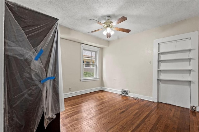 unfurnished bedroom featuring visible vents, hardwood / wood-style floors, baseboards, a textured ceiling, and a ceiling fan