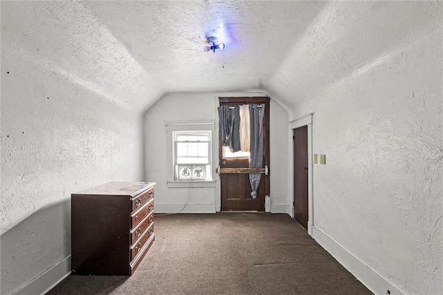 additional living space featuring a textured wall, dark colored carpet, a textured ceiling, and lofted ceiling