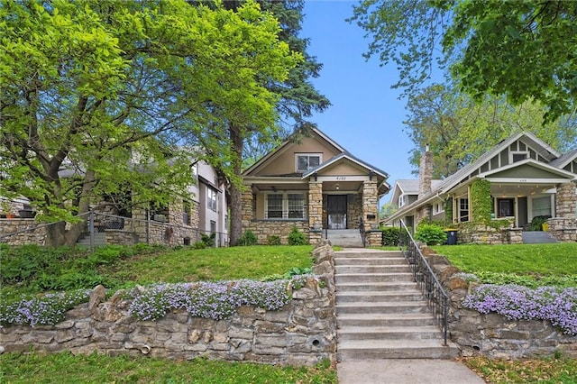 craftsman house featuring a front lawn, fence, covered porch, and stone siding