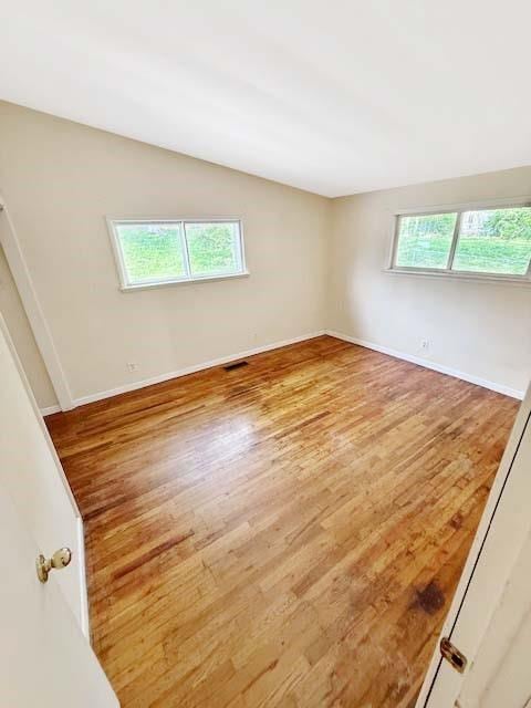 unfurnished room with baseboards, wood finished floors, and visible vents