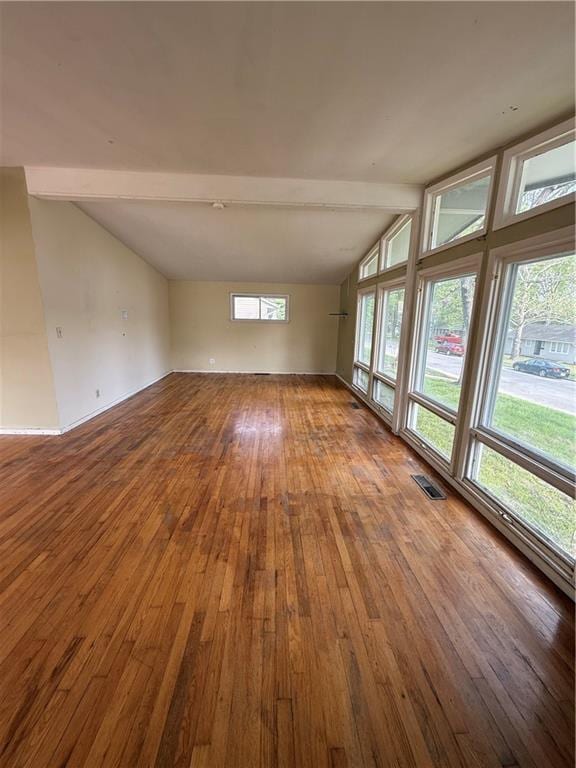 empty room featuring lofted ceiling with beams, hardwood / wood-style flooring, and visible vents