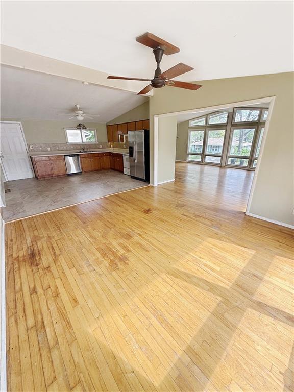 unfurnished living room with a ceiling fan, light wood-style flooring, lofted ceiling, and a healthy amount of sunlight