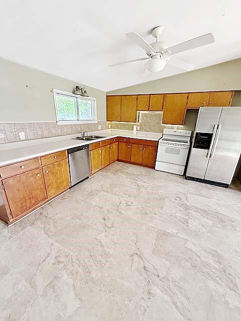 kitchen with light countertops, brown cabinets, tasteful backsplash, appliances with stainless steel finishes, and vaulted ceiling