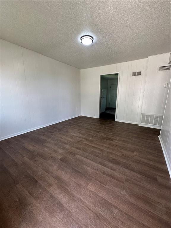 unfurnished room featuring dark wood-type flooring, a textured ceiling, visible vents, and baseboards