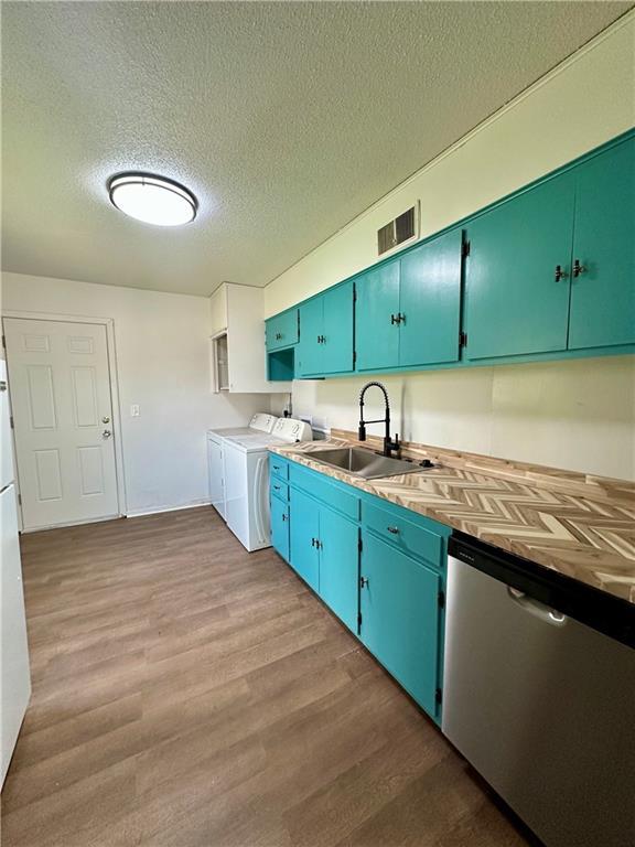 kitchen with dishwasher, visible vents, wood finished floors, a sink, and washing machine and clothes dryer