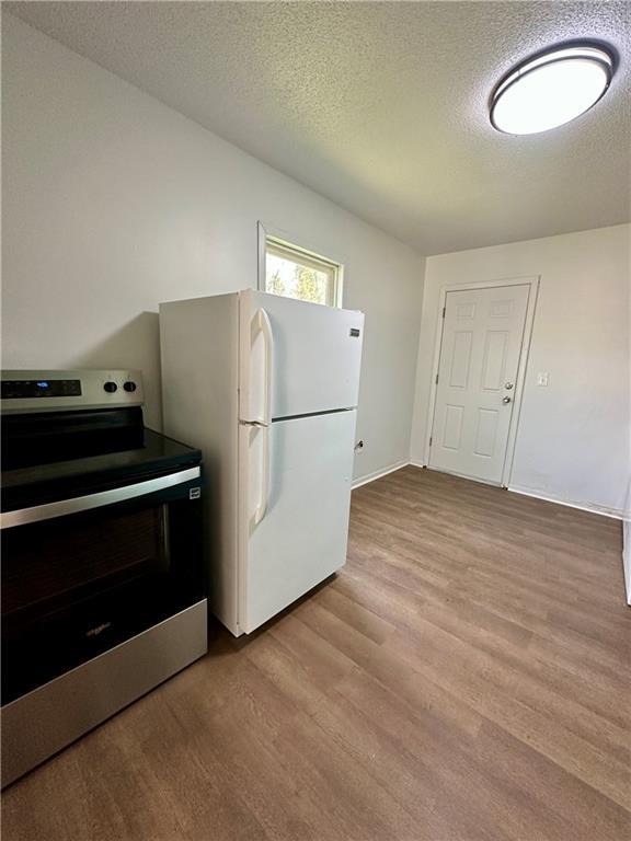 kitchen with wood finished floors, freestanding refrigerator, baseboards, a textured ceiling, and stainless steel electric range oven