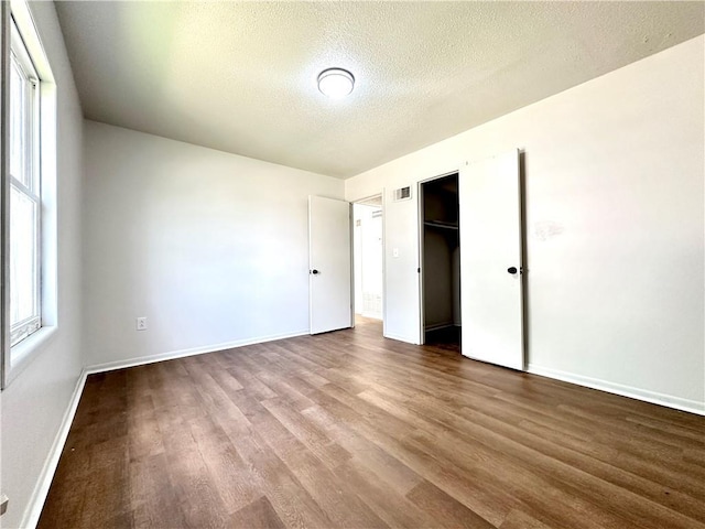 unfurnished bedroom featuring wood finished floors, visible vents, a closet, baseboards, and a textured ceiling
