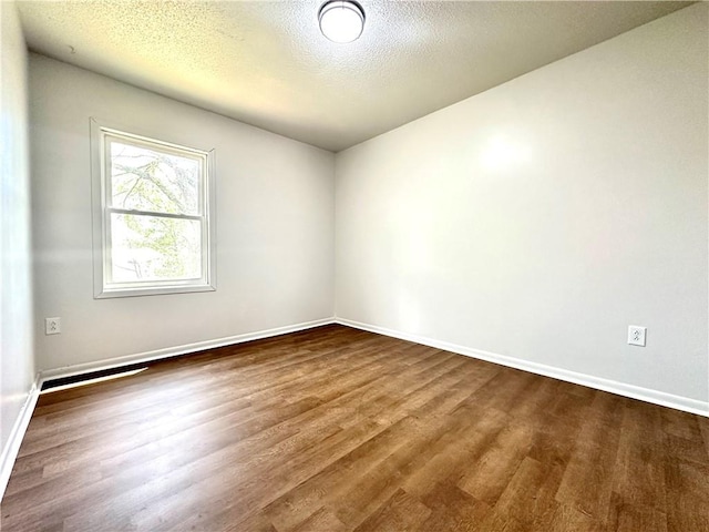 spare room with baseboards, a textured ceiling, and dark wood-type flooring