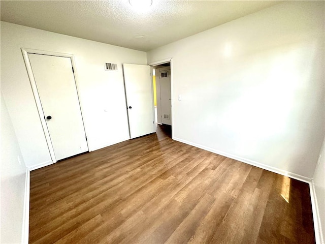 unfurnished bedroom with visible vents, baseboards, wood finished floors, and a textured ceiling