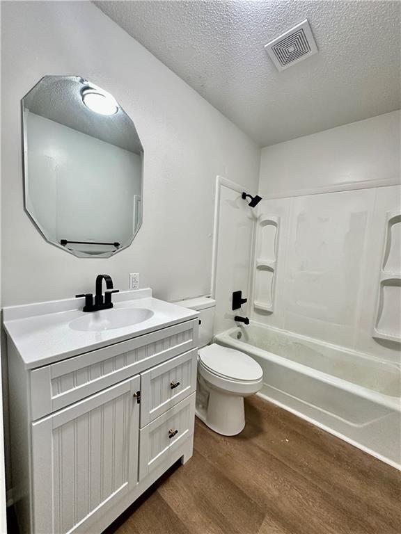 full bathroom with wood finished floors, visible vents, toilet, vanity, and a textured ceiling