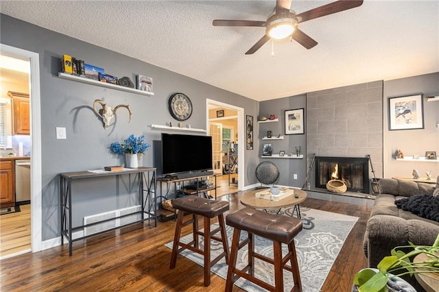 living room featuring a textured ceiling, ceiling fan, wood finished floors, and a fireplace