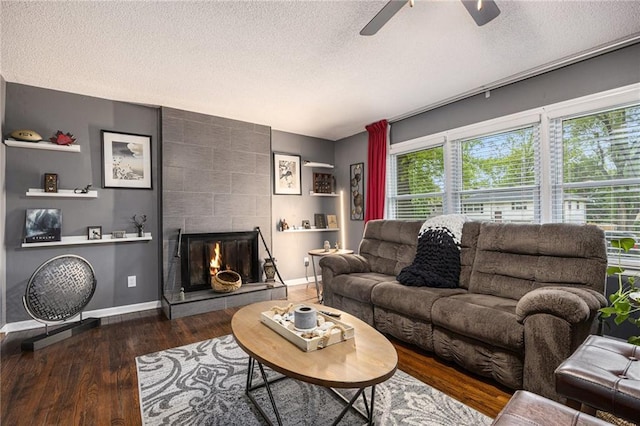 living room featuring wood finished floors, a fireplace, baseboards, ceiling fan, and a textured ceiling