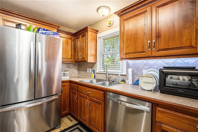 kitchen featuring a textured ceiling, brown cabinets, a sink, backsplash, and stainless steel appliances