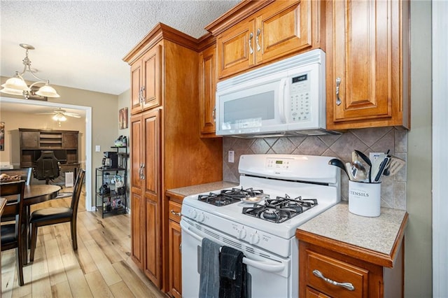kitchen featuring ceiling fan, brown cabinets, light countertops, light wood finished floors, and white appliances