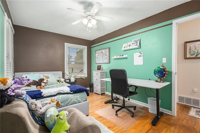 bedroom with a textured ceiling, ceiling fan, wood finished floors, and visible vents
