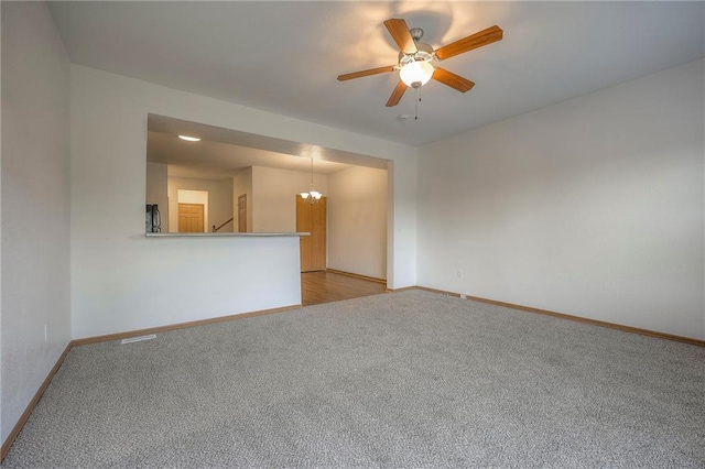 empty room with baseboards, visible vents, ceiling fan with notable chandelier, and light colored carpet