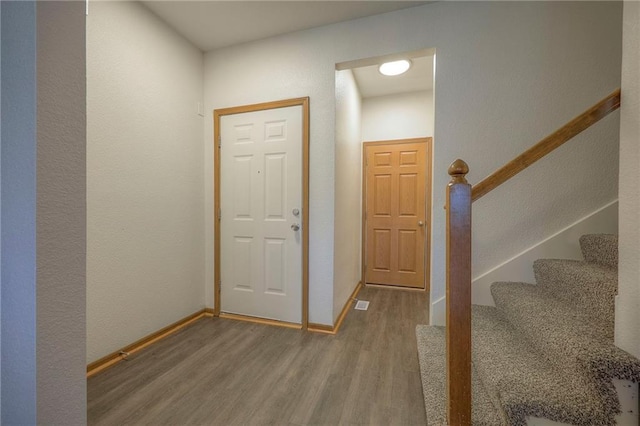foyer with baseboards, stairs, wood finished floors, and visible vents