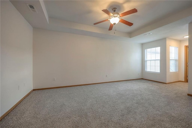 carpeted spare room featuring visible vents, a ceiling fan, a raised ceiling, and baseboards