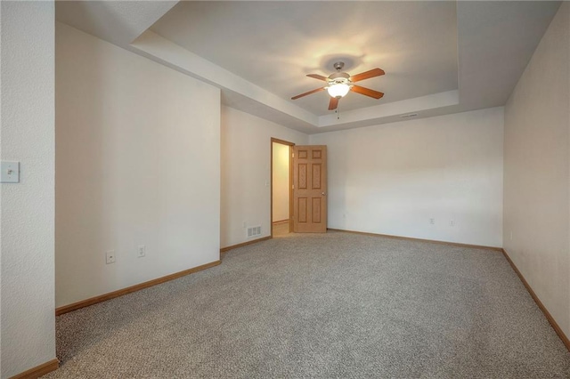 spare room with a raised ceiling, ceiling fan, carpet flooring, and visible vents