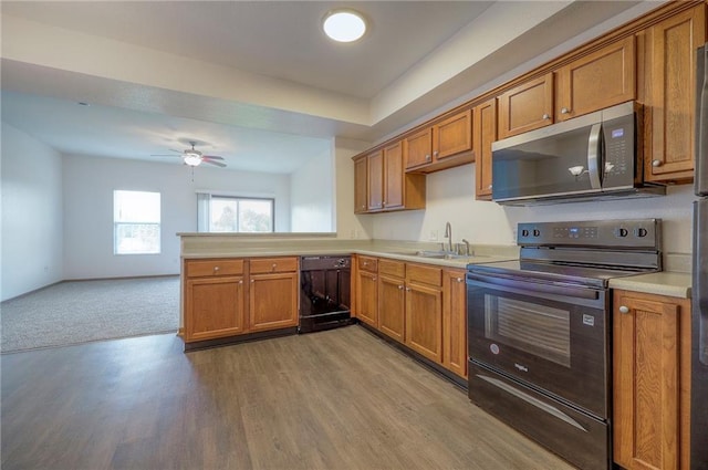 kitchen with light countertops, brown cabinetry, a sink, and black appliances