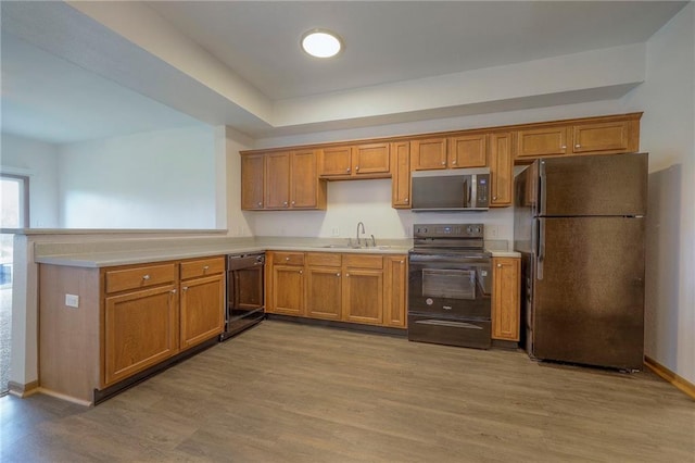 kitchen with brown cabinets, a sink, light wood-style floors, light countertops, and black appliances