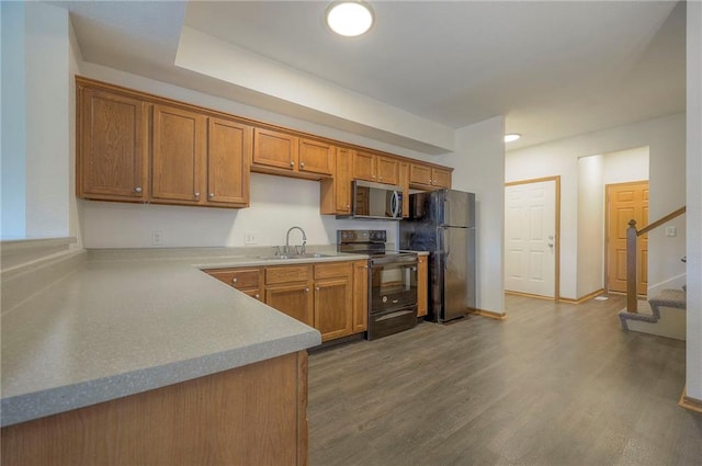 kitchen with a sink, dark wood finished floors, brown cabinets, and black appliances