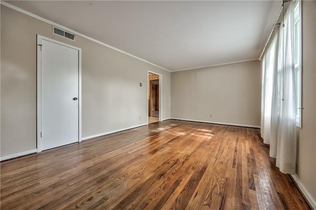 spare room featuring crown molding, baseboards, wood finished floors, and visible vents