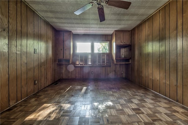 empty room featuring baseboards, ceiling fan, and wood walls