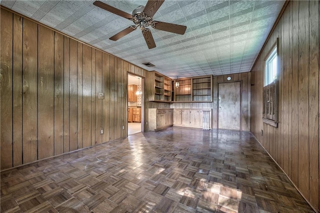 unfurnished living room with wooden walls, baseboards, ceiling fan, and visible vents