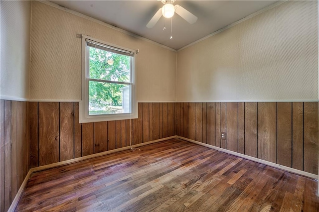spare room with a wainscoted wall, ornamental molding, wood-type flooring, and ceiling fan