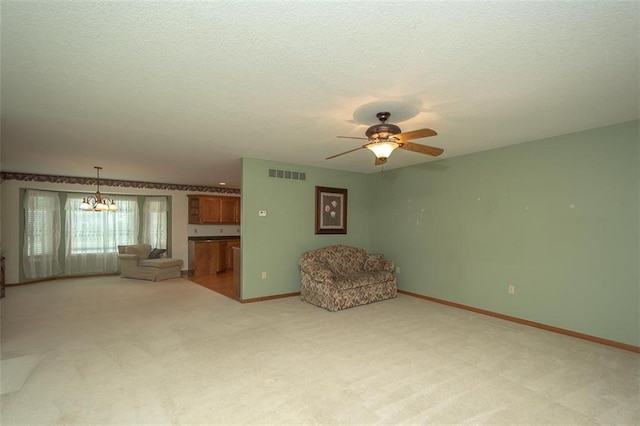 unfurnished room featuring visible vents, baseboards, a textured ceiling, light colored carpet, and ceiling fan with notable chandelier