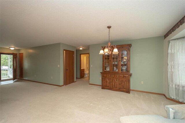 unfurnished living room featuring a textured ceiling, a notable chandelier, baseboards, and light carpet