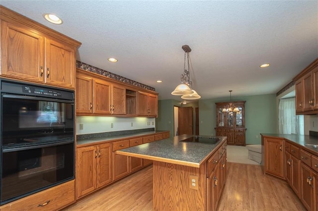 kitchen featuring a center island, black appliances, light wood finished floors, and dark countertops
