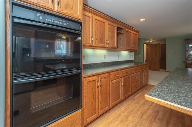 kitchen with light wood-type flooring, dark countertops, brown cabinets, and dobule oven black