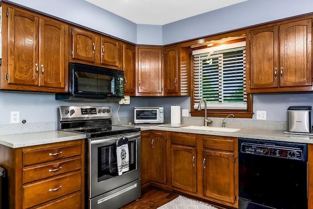 kitchen featuring black appliances, a sink, light countertops, and brown cabinetry