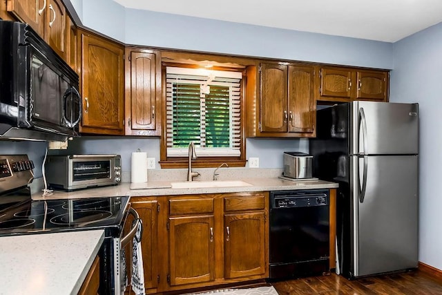 kitchen featuring black appliances, a sink, light countertops, dark wood-style flooring, and brown cabinetry
