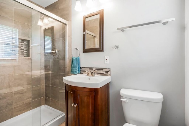 bathroom featuring a shower stall, toilet, vanity, and backsplash