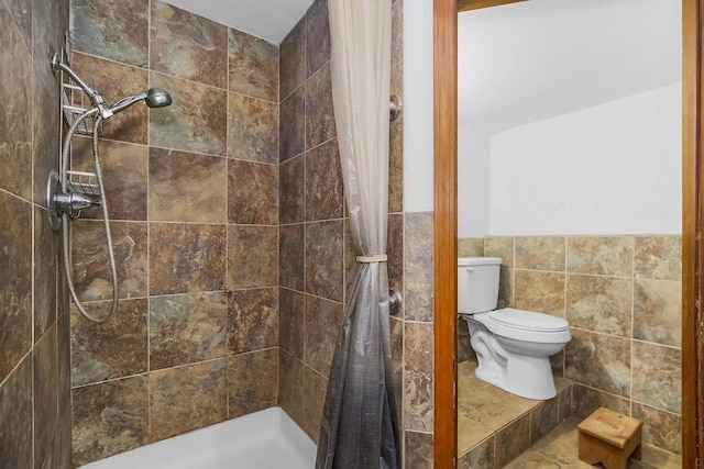 full bath with tile walls, tiled shower, toilet, and a wainscoted wall